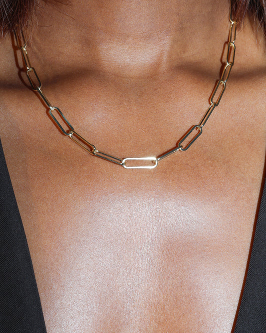 Gold paperclip chain necklace on a person's neck with a blurred background