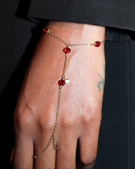 Gold Hand Harness with red gemstones on a person's hand against a black background