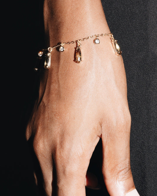 Hand wearing a gold bracelet with small charms against a black background
