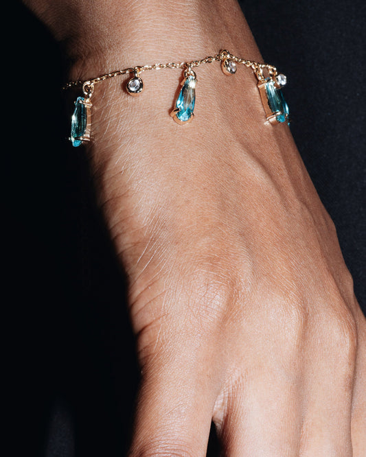 Bracelet with light blue teardrop-shaped gemstones on a wrist against a dark background