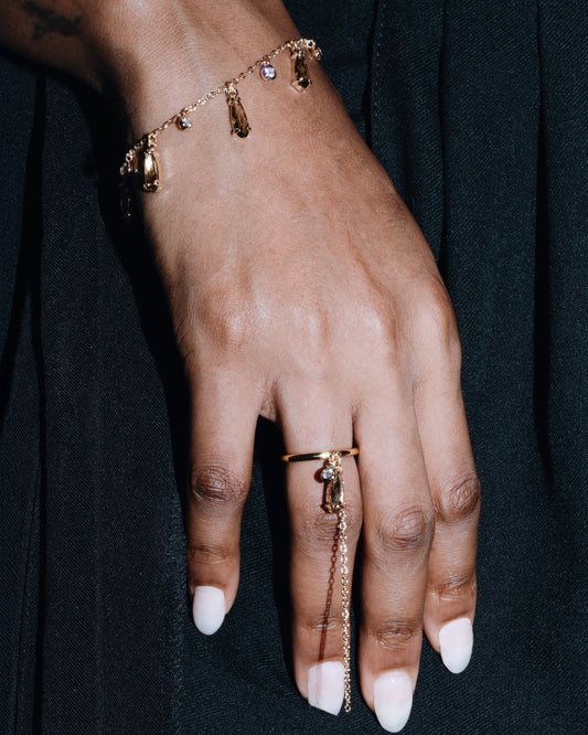 Hand wearing a gold bracelet and ring on a dark background