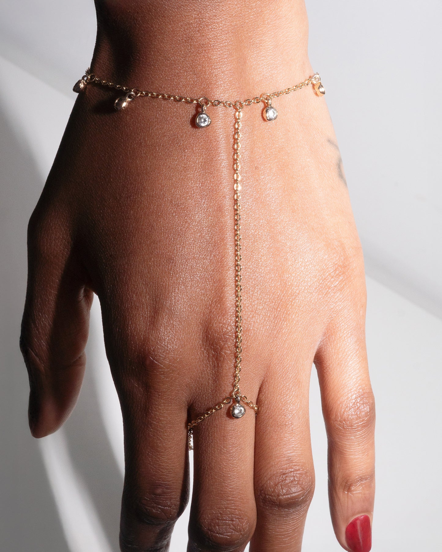Gold filled hand harness with crystal bezel charms by Studio Baloge, draped elegantly on a woman's hand. Dainty chain connecting wrist to finger, luxury minimalist jewelry handcrafted in New York.
