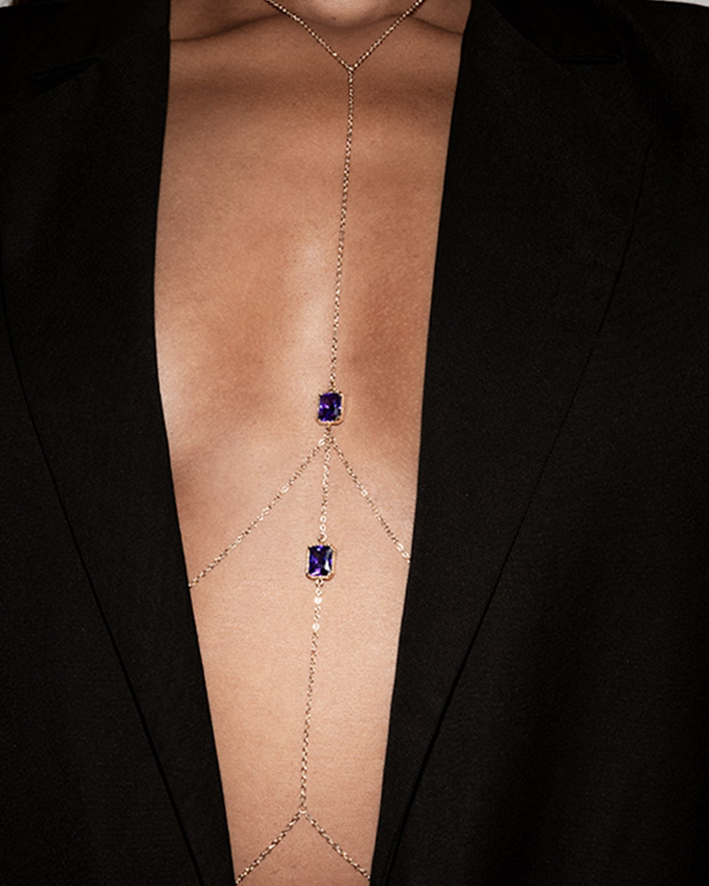 Gold body chain with purple gemstones worn by a person in a black blazer.