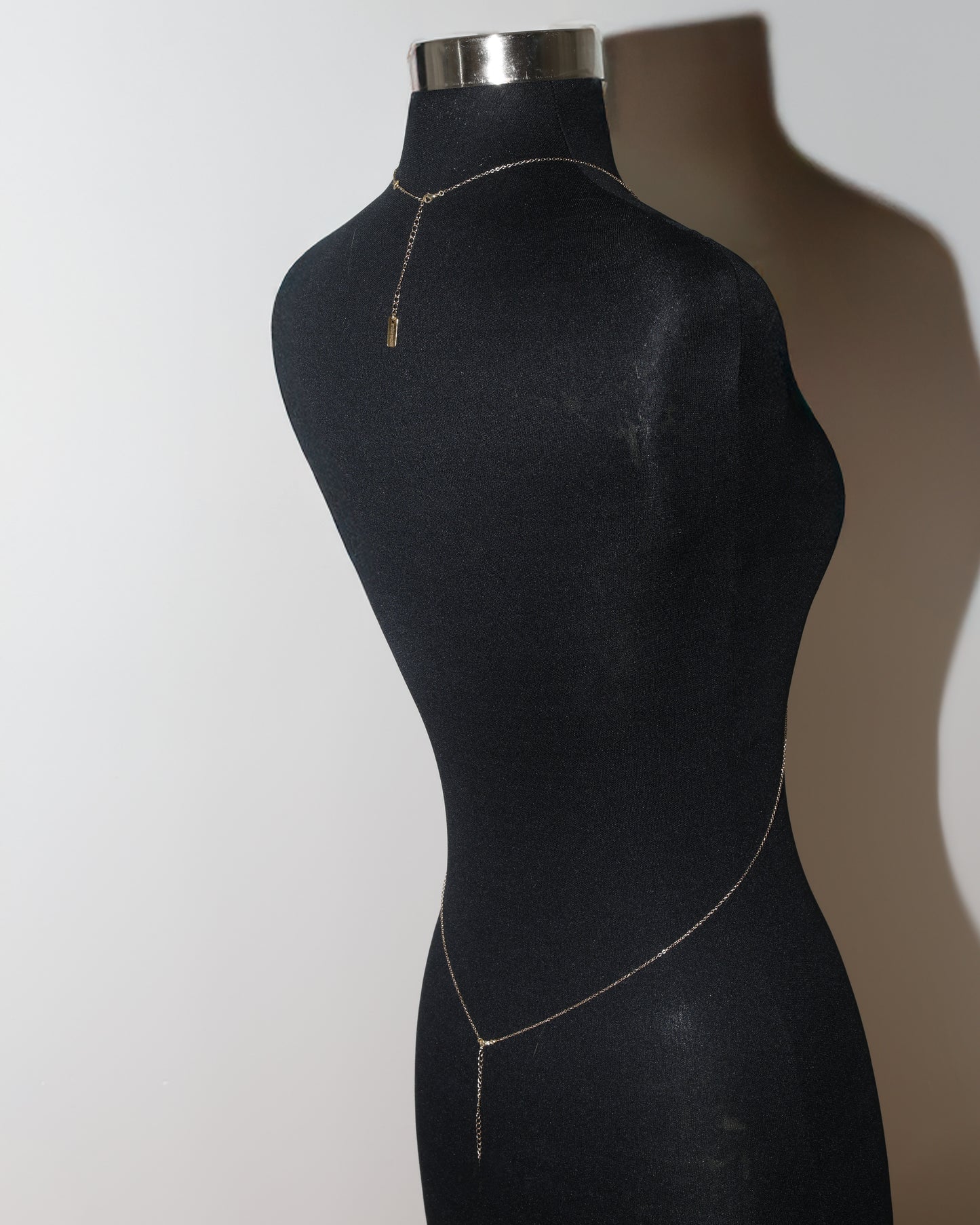 Mannequin wearing a delicate gold body chain against a plain background