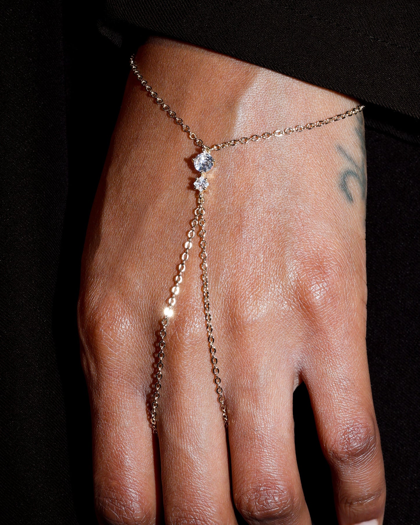 Hand wearing a delicate gold chain bracelet with small stones on a dark background