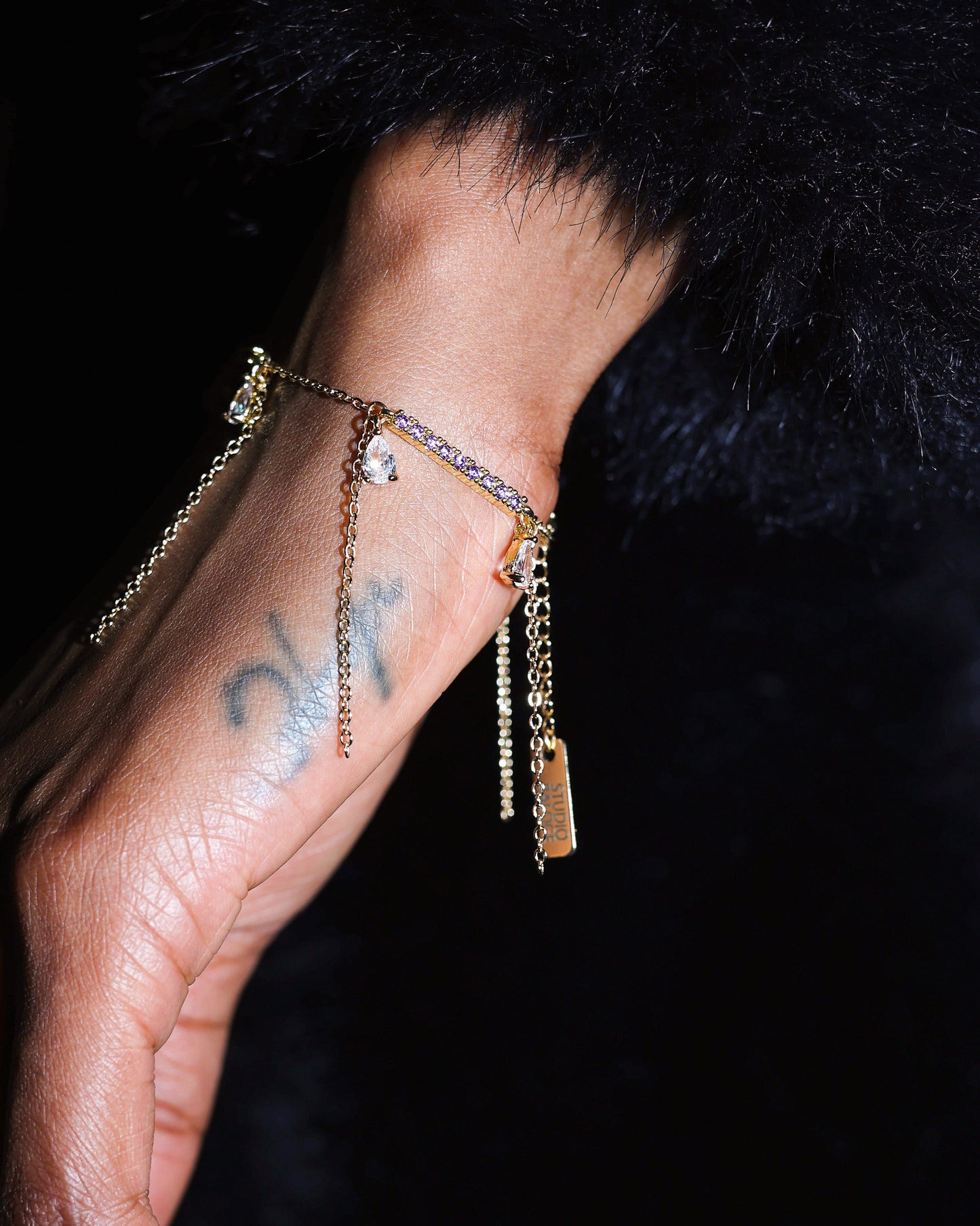 Hand wearing a delicate bracelet with small charms against a dark background