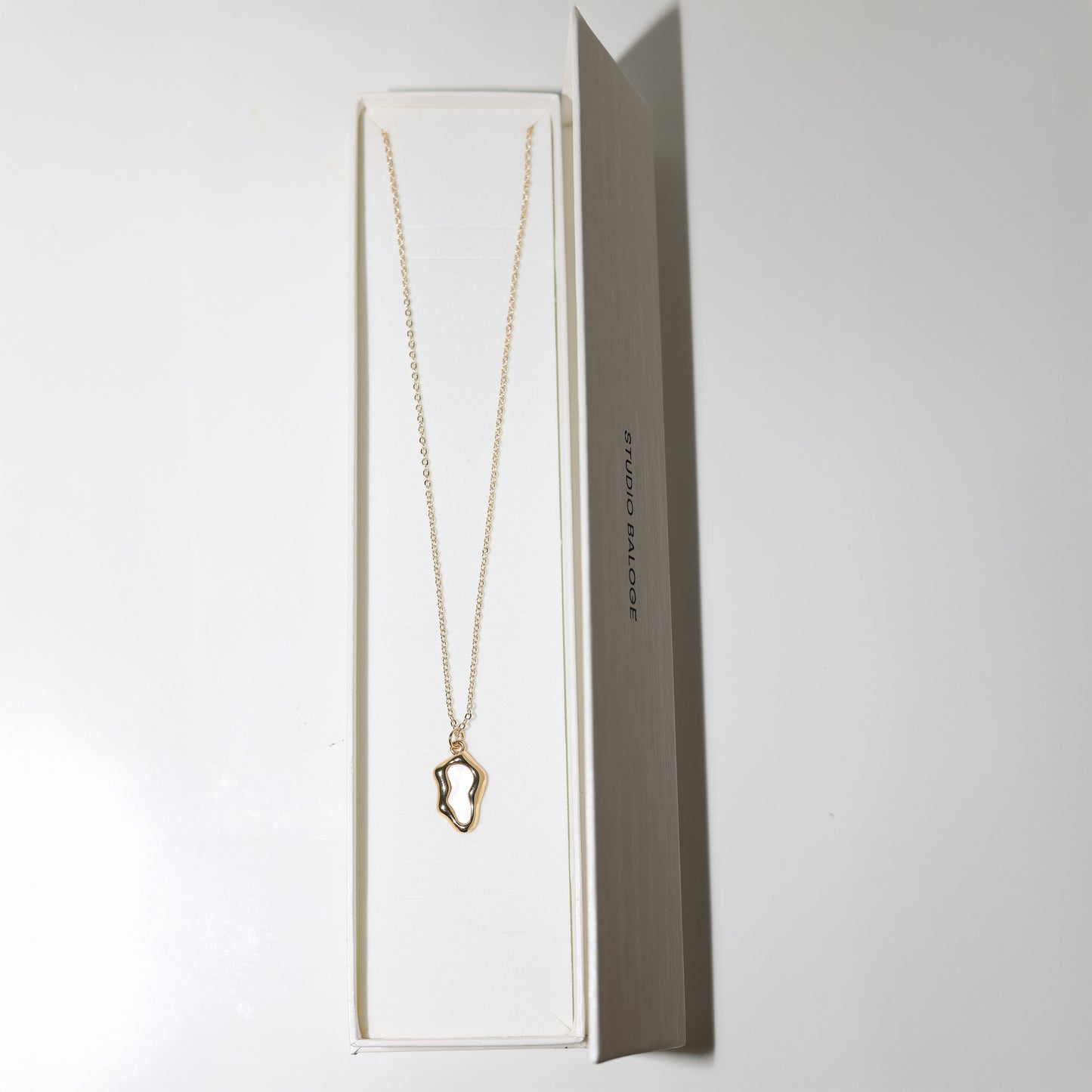 Gold necklace with a unique pendant in Studio Baloge open jewelry box on a white background