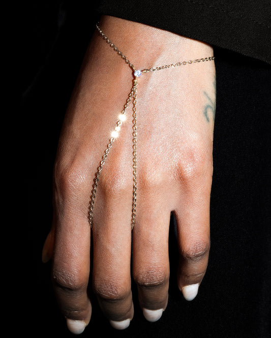 Hand wearing a delicate gold chain bracelet on a black background