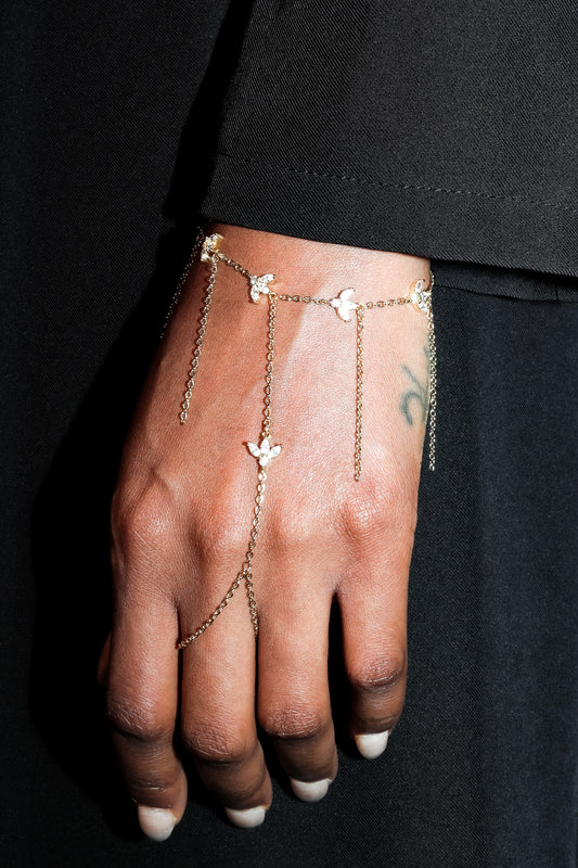 Hand wearing a delicate gold chain bracelet with small floral charms against a black background