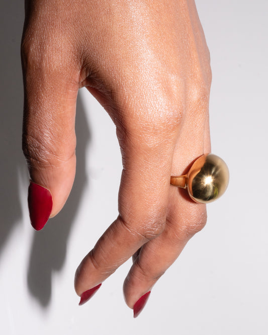 Soléa Ring on hand – smooth sculptural dome in high-polish gold, styled with red nails, photographed against a white backdrop.