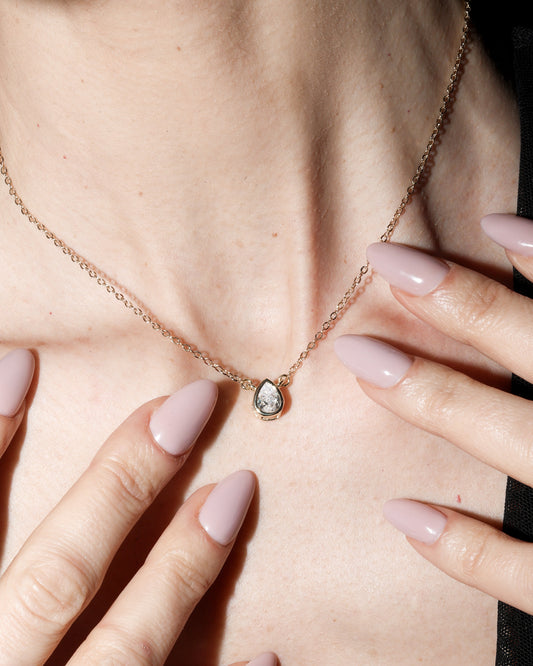 Necklace with a green gemstone worn by a person, with hands gently touching the skin.