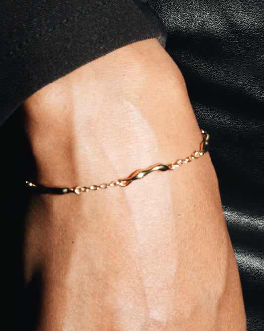 Gold bracelet on a wrist with a black background
