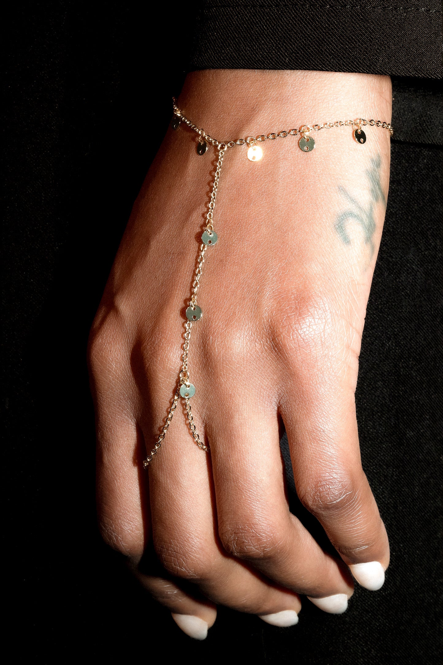 Hand wearing a delicate bracelet with small gold discs on a black background