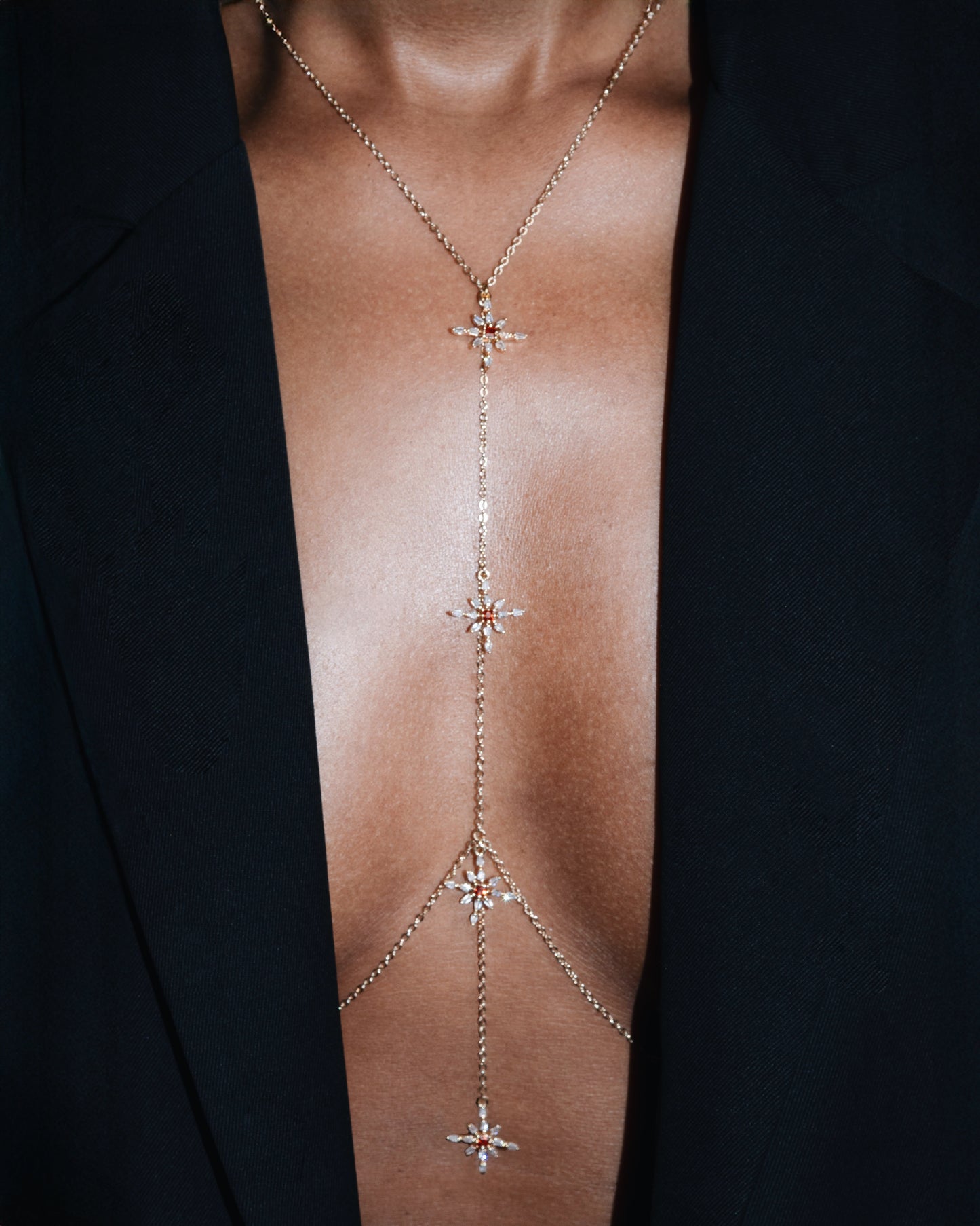 Delicate gold body chain with star designs on a person wearing a black garment.