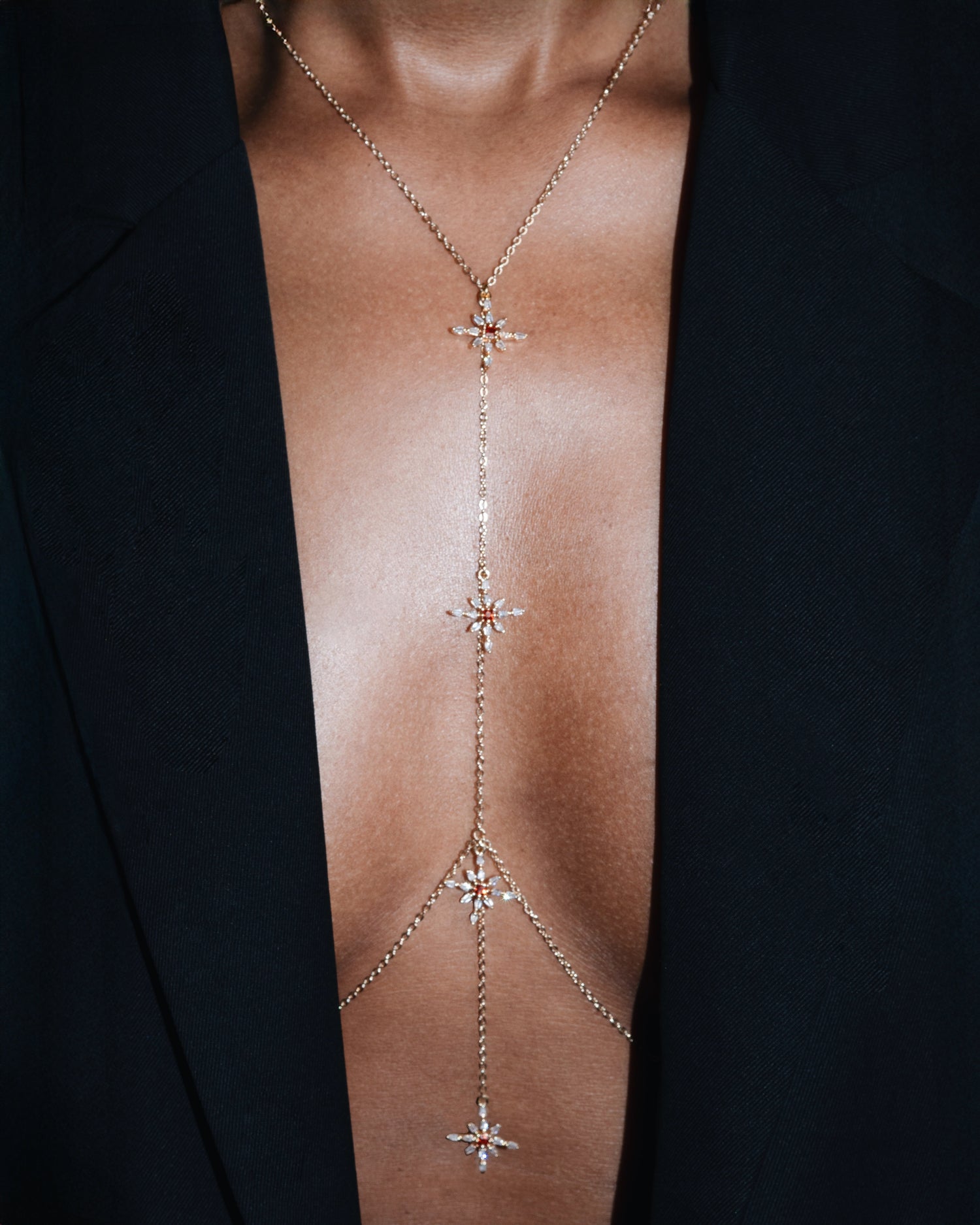 Delicate gold body chain with star designs on a person wearing a black garment.