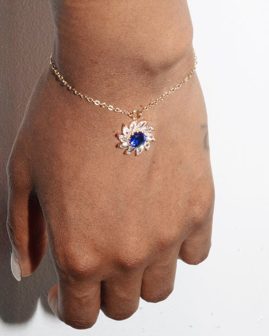 Gold bracelet with a blue gemstone on a person's ankle against a neutral background