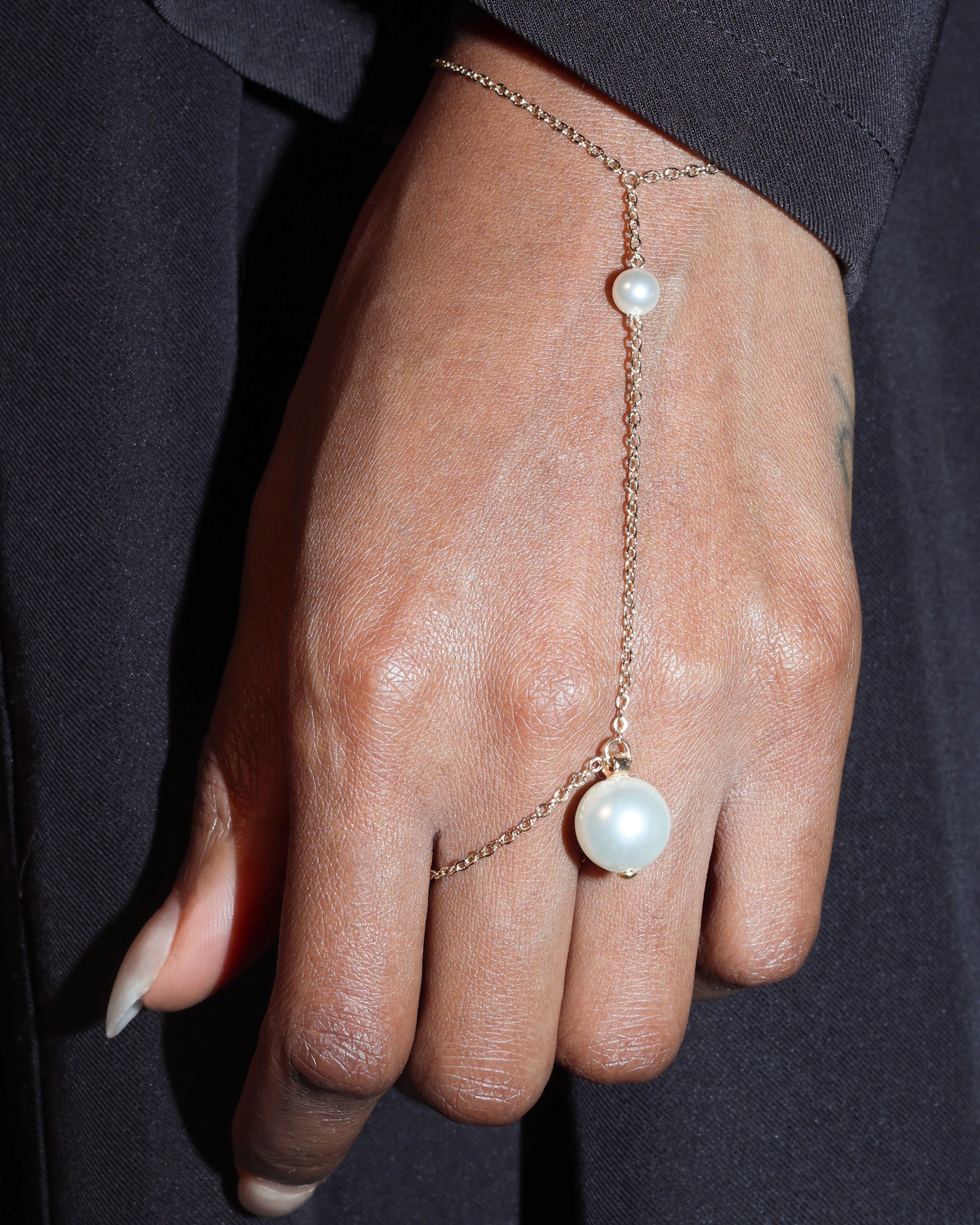 Hand wearing a delicate gold chain bracelet with pearl-like stones against a dark background