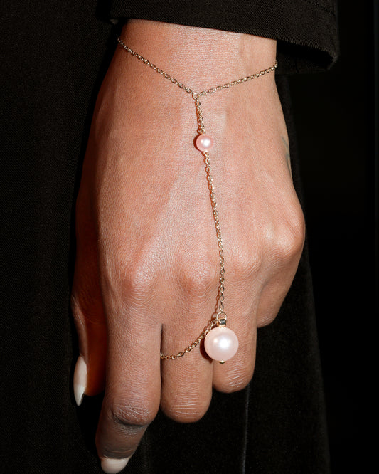 Hand wearing a delicate gold chain with pink pearls against a black background