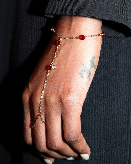 Hand wearing a delicate hand chain bracelet with red gemstones against a dark background