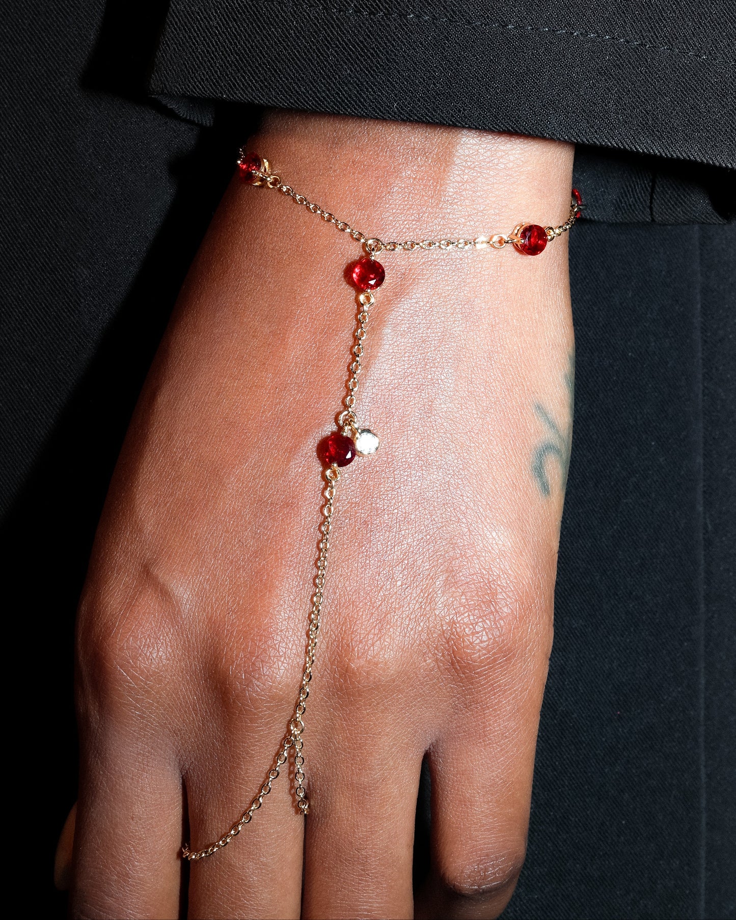 Gold Hand Harness with red gemstones on a person's hand against a black background