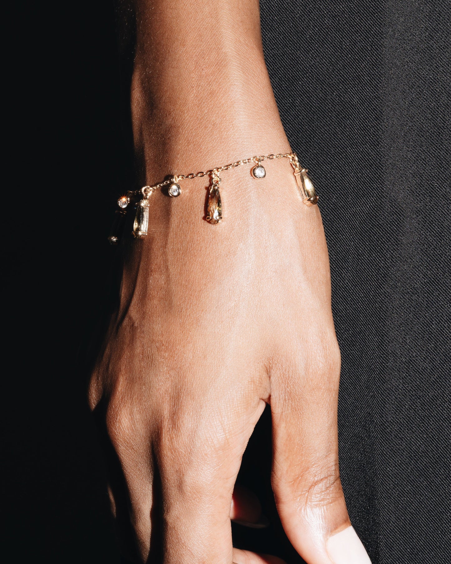 Hand wearing a gold bracelet with small charms against a black background