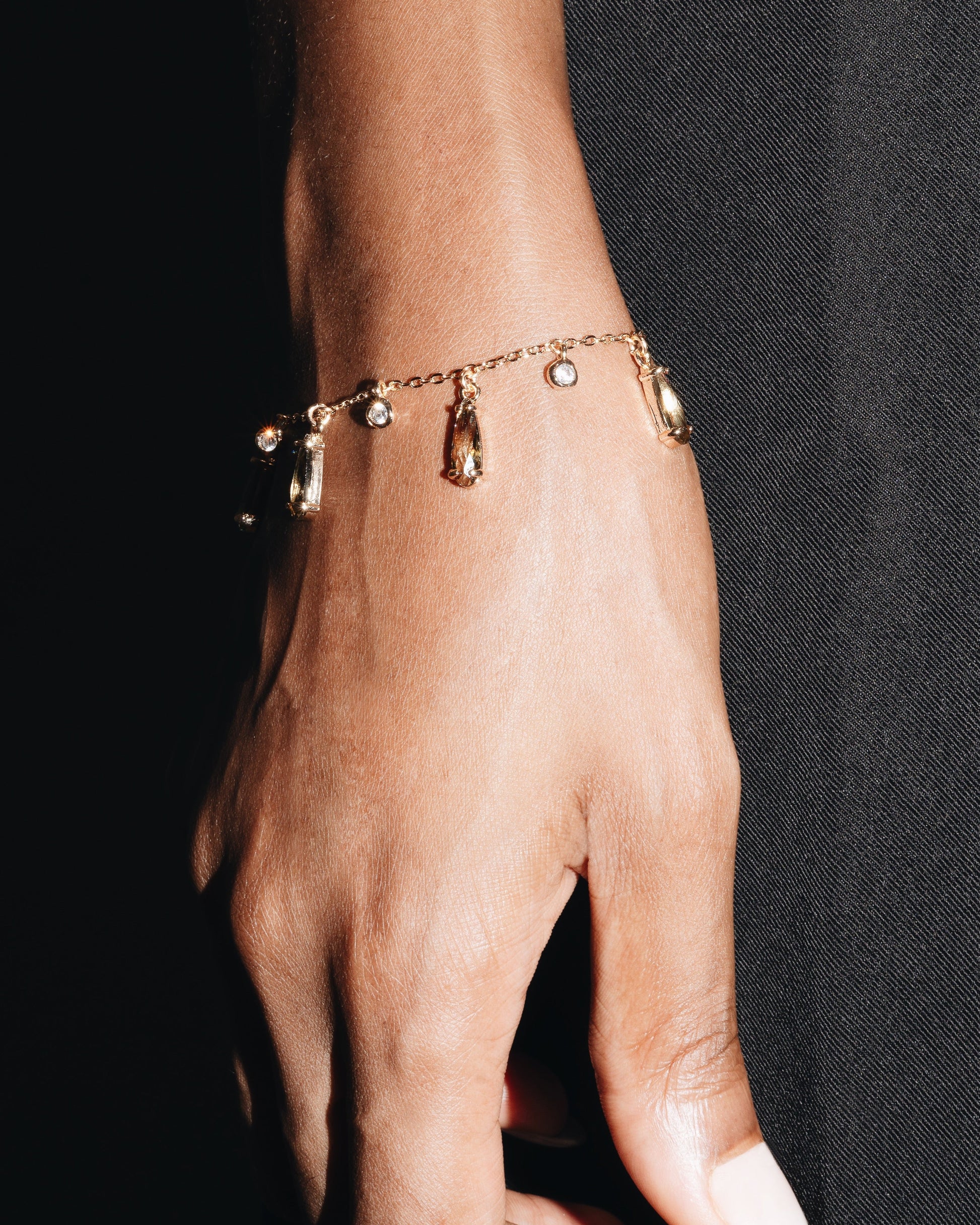 Hand wearing a gold bracelet with small charms against a black background