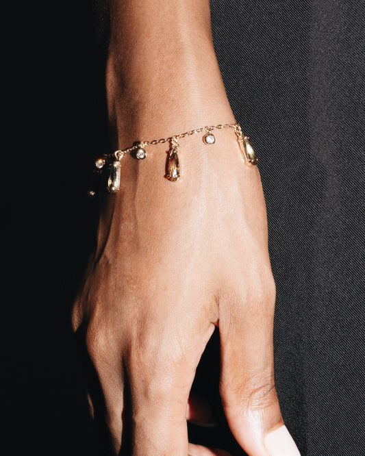 Hand wearing a gold bracelet with small charms against a black background