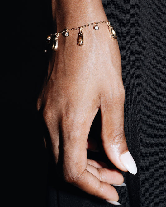 Hand wearing a gold bracelet with small charms against a black background