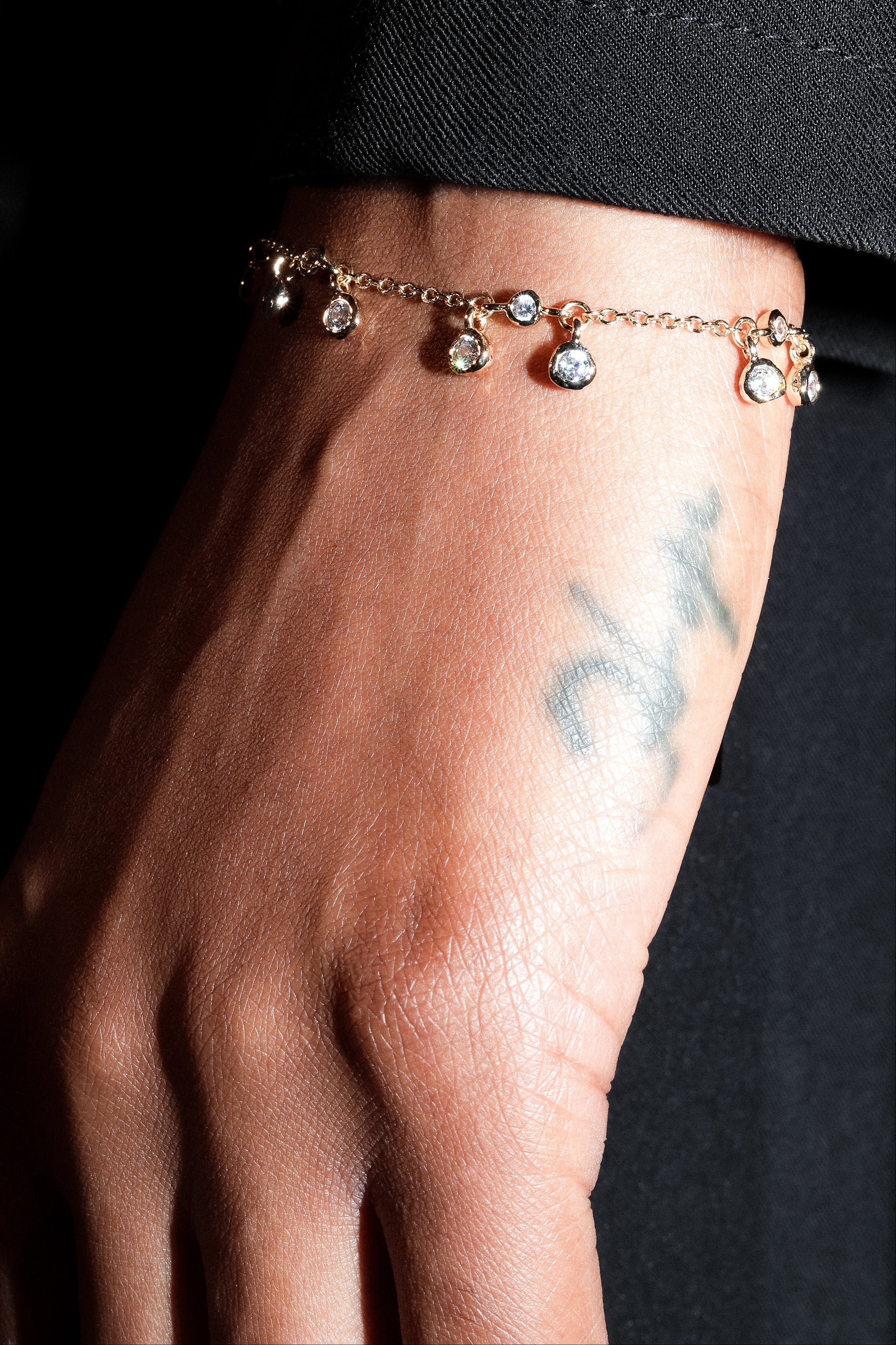 Close-up of a hand wearing a delicate bracelet with small charms against a dark background