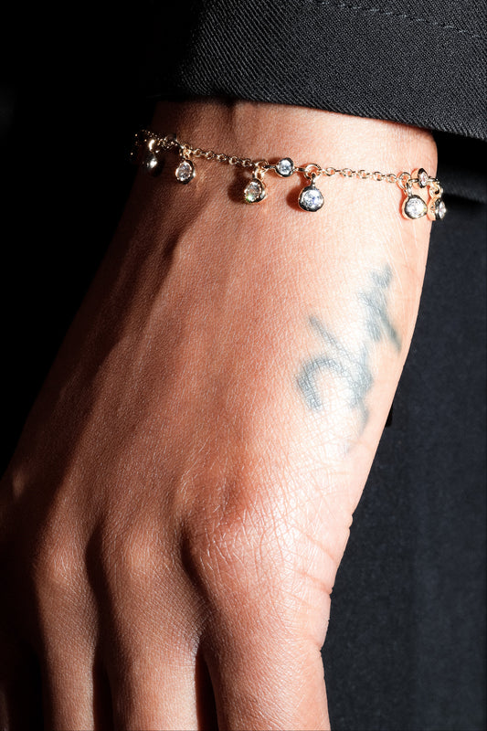 Close-up of a hand wearing a delicate bracelet with small charms against a dark background