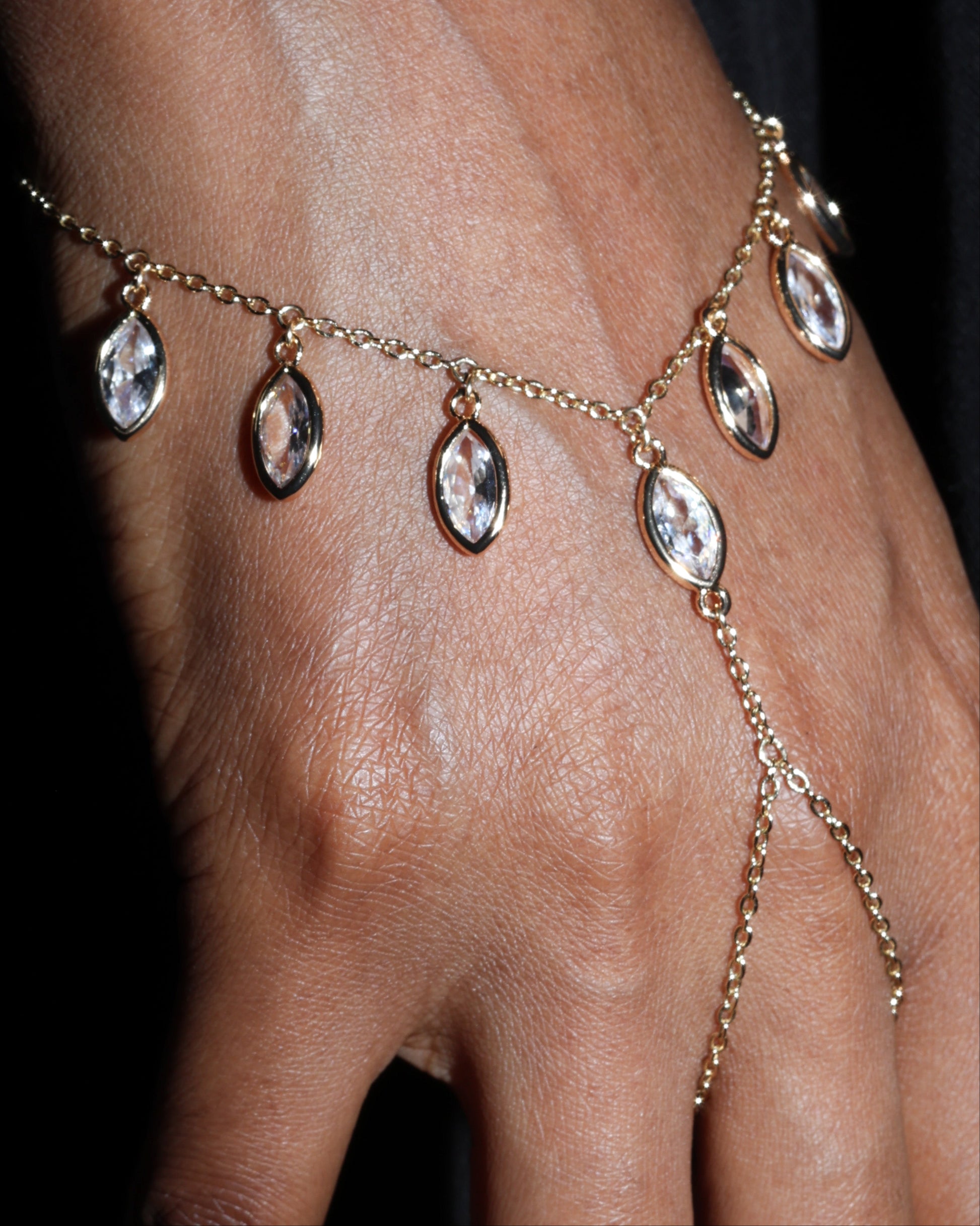 Gold chain bracelet with teardrop-shaped crystals on a wrist against a black background
