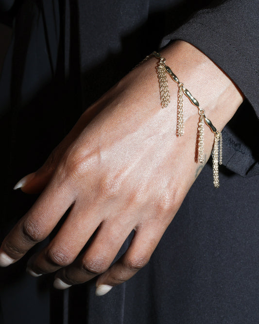 Close-up of a hand wearing a gold bracelet with chain tassels against a dark background