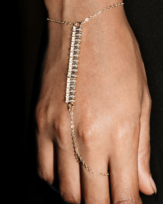Gold hand chain on a person's hand against a black background