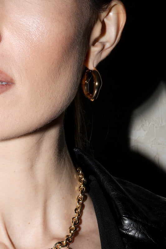 Close-up of a person wearing a gold necklace and earrings with a black leather jacket.