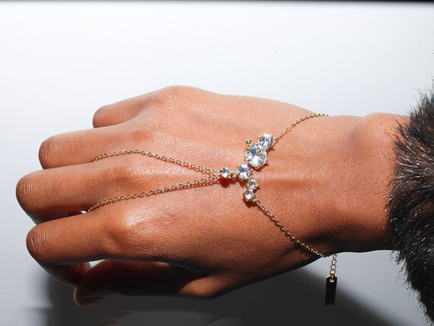 Hand wearing a delicate gold bracelet with small stones on a neutral background