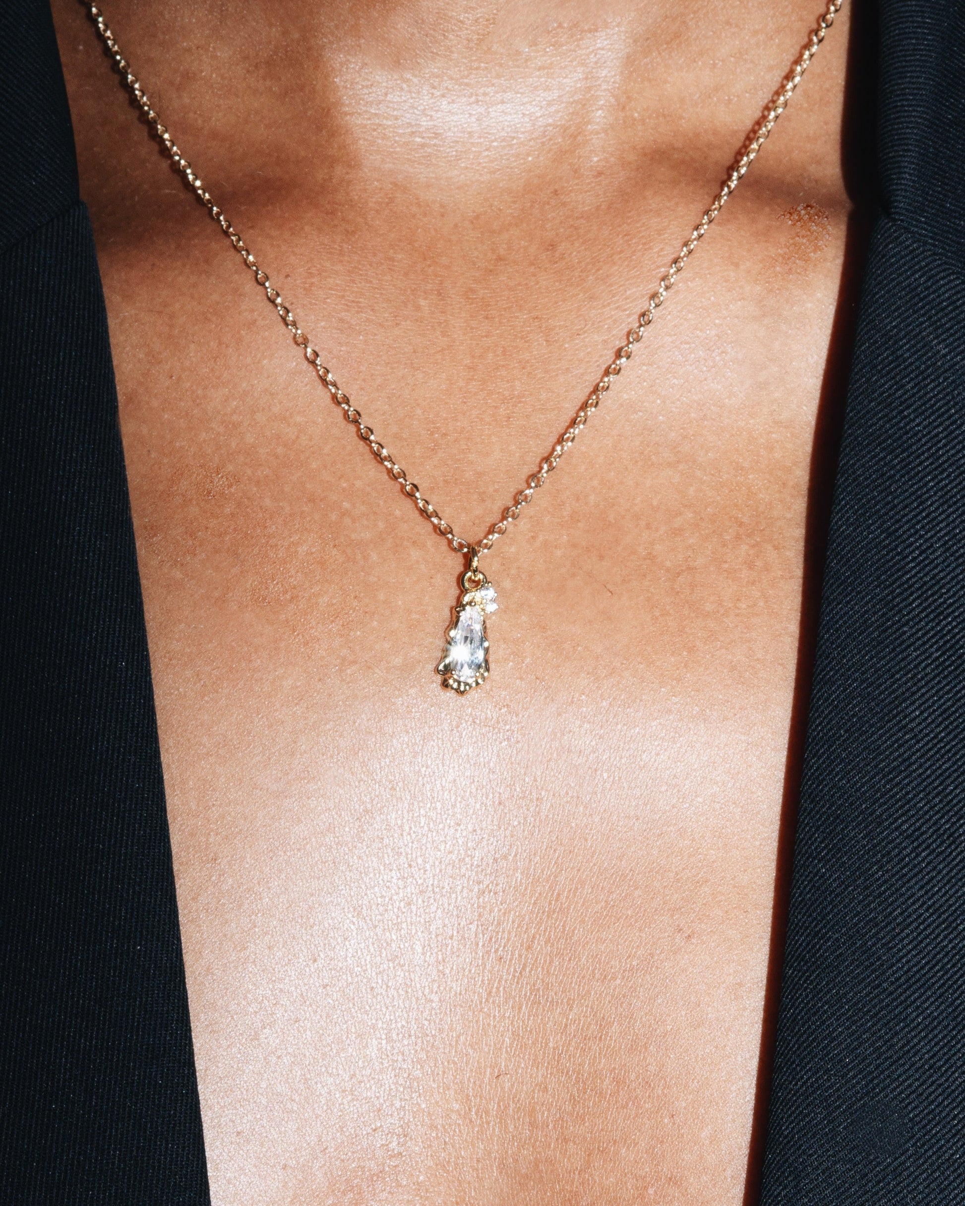 Gold necklace with a pendant on a person wearing a black blazer.
