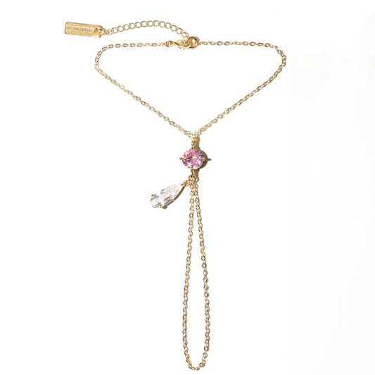 Gold hand chain with a pink gemstone pendant on a white background