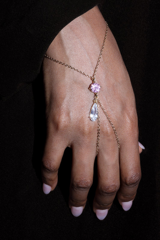 Hand wearing a delicate gold chain with bright pinkgemstones against a black background