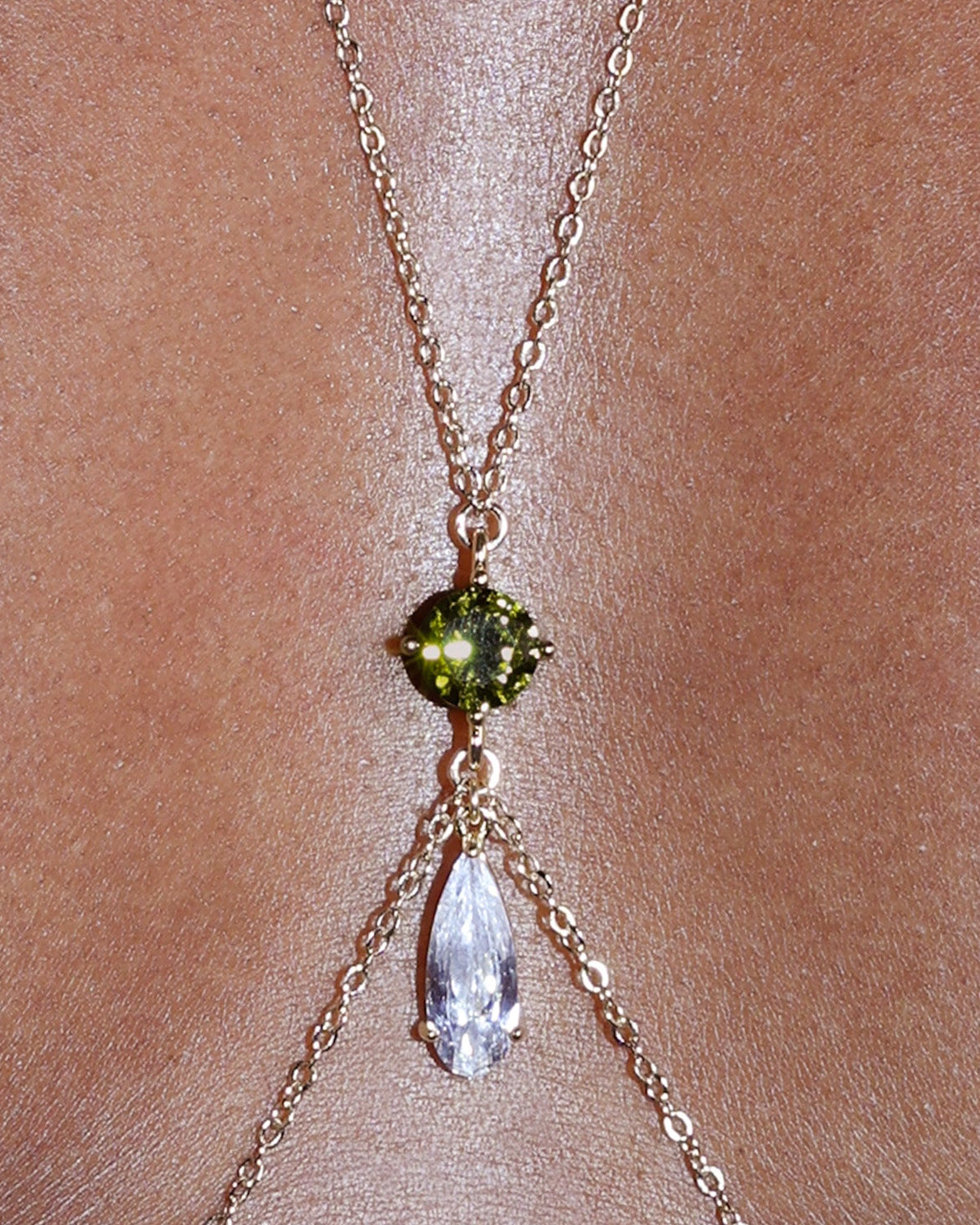 Gold body chain with a green gemstone on a person wearing a black garment.