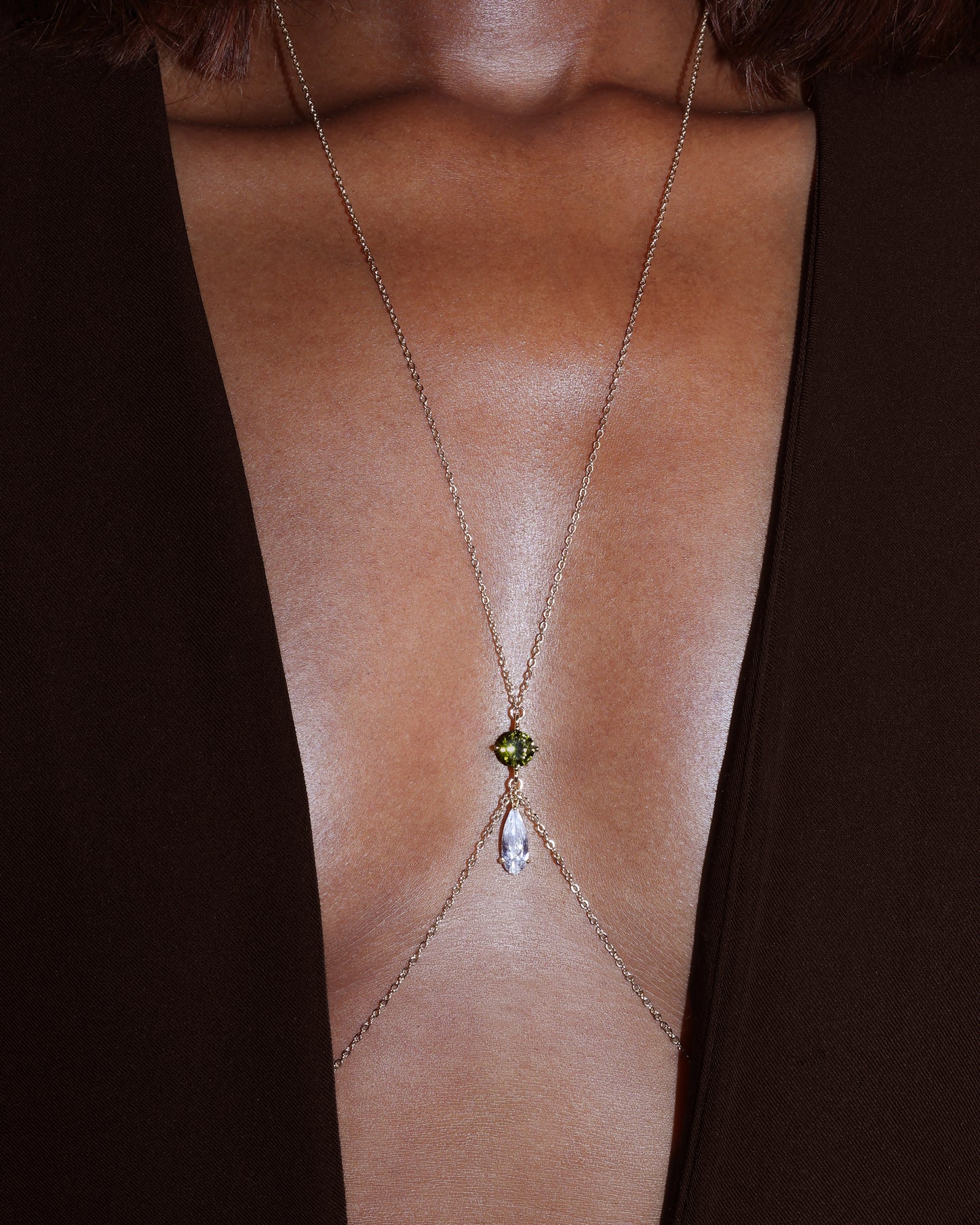 Gold body chain with a green gemstone on a person wearing a black garment.