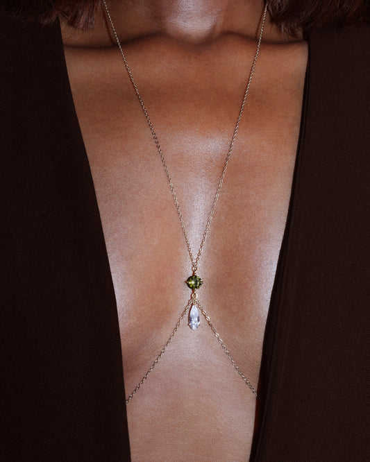 Gold body chain with a green gemstone on a person wearing a black garment.