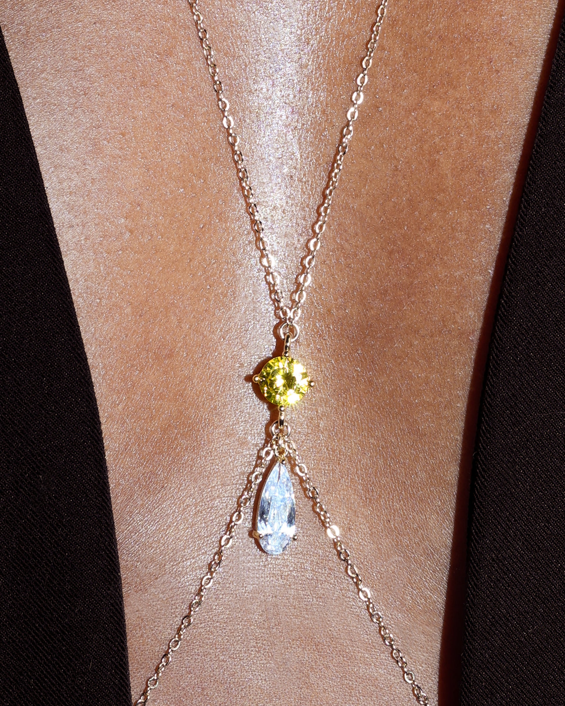 Body chain with gemstones on a person's skin against a dark background