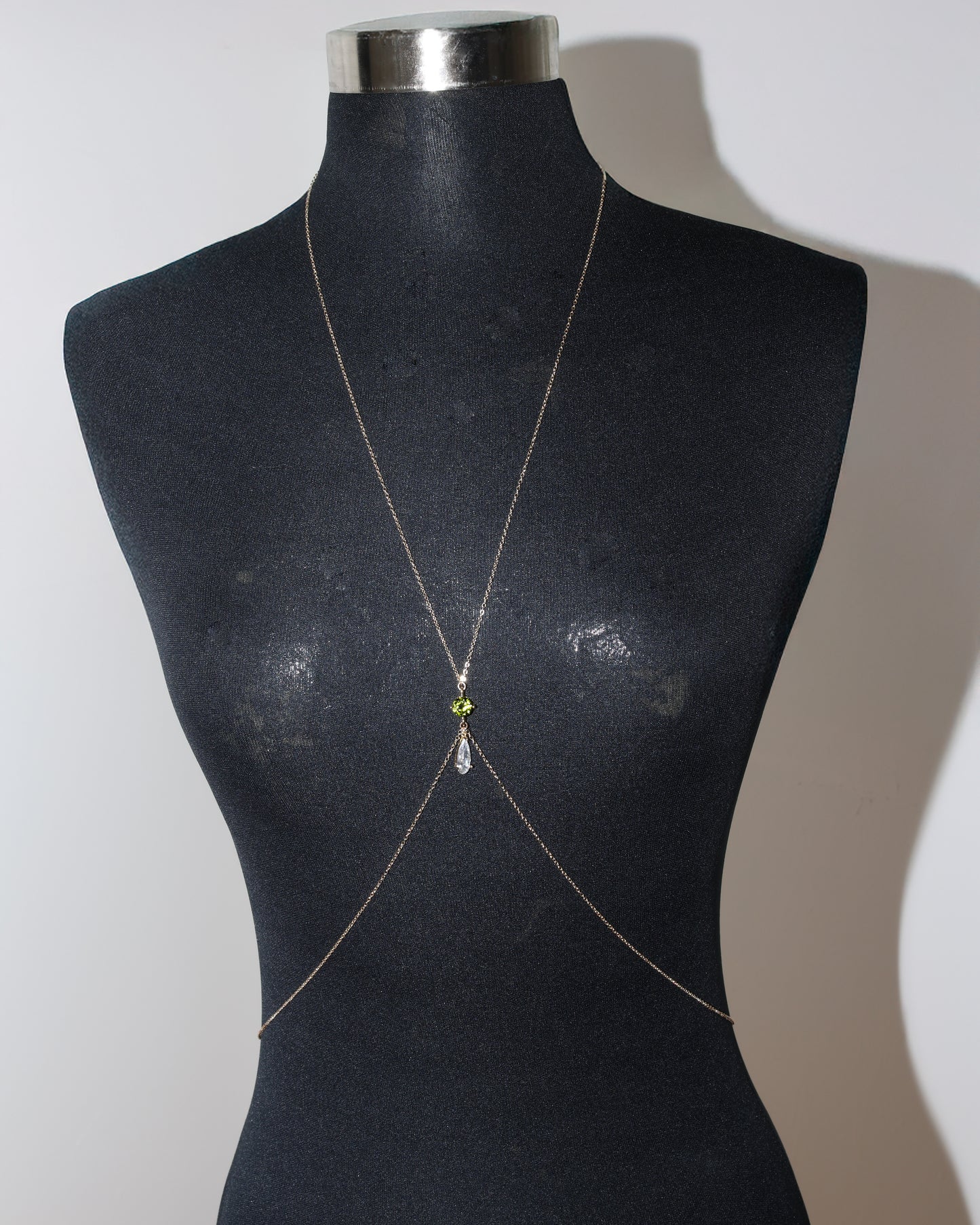 Gold body chain with a green gemstone on a black mannequin against a white background