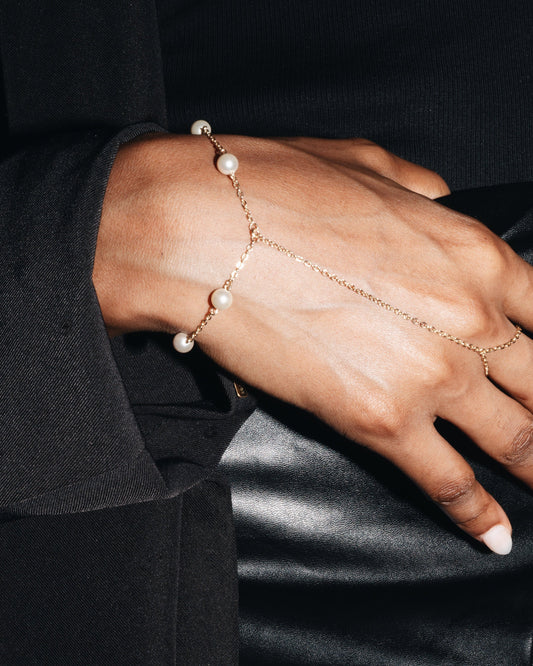 Close-up of a hand wearing a delicate hand harness with luxurious pearls with a black elegant outfit