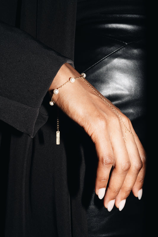 Hand wearing a Studio Baloge delicate hand harness bracelet with white pearls with model wearing black outfit 