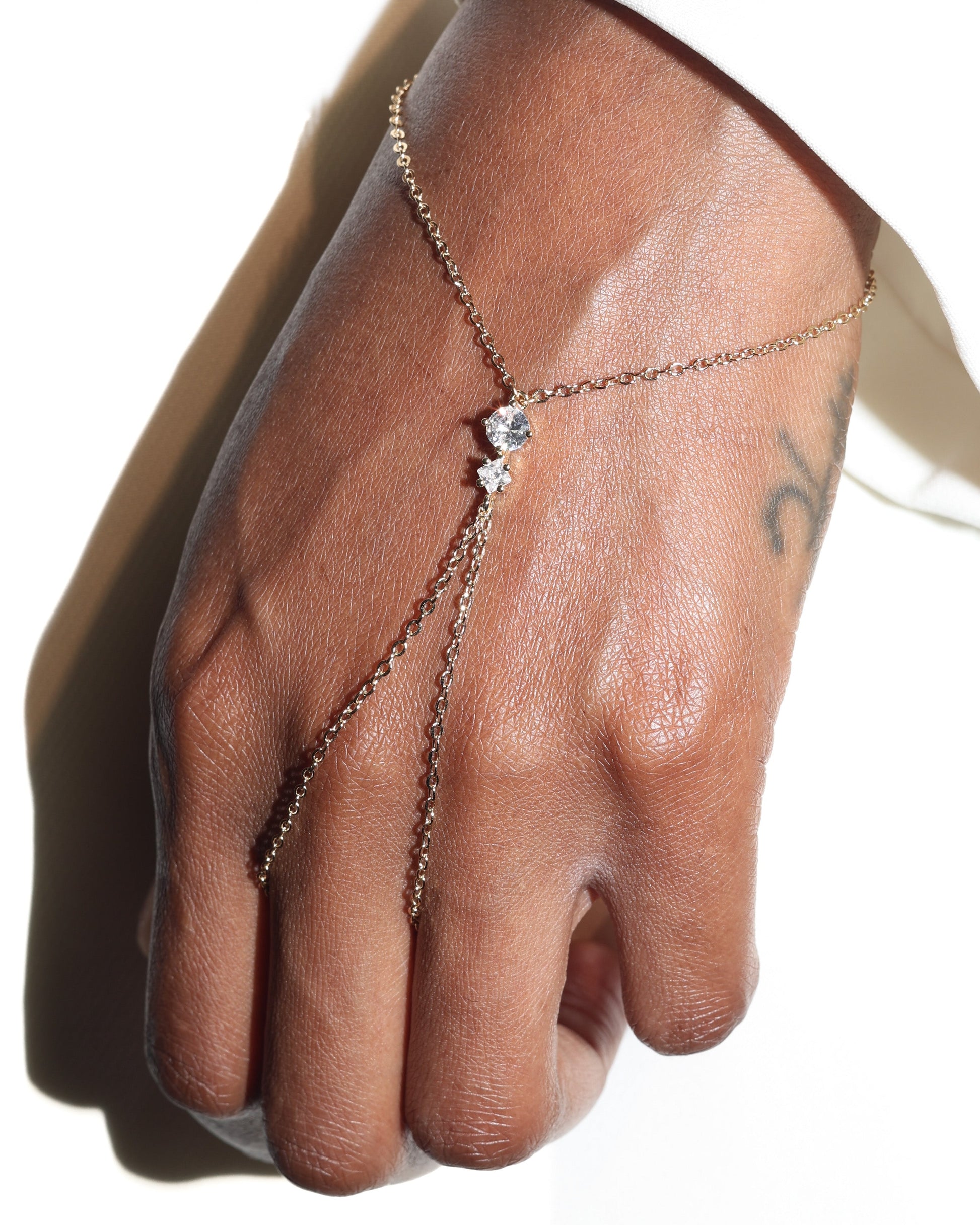 Hand wearing a delicate chain bracelet with a small diamond on a neutral background