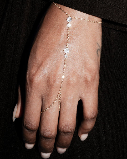 Hand wearing a delicate gold bracelet with small stones on a dark background