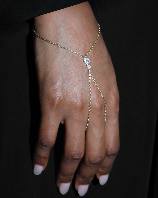 Hand wearing a delicate gold bracelet with a central gemstone against a black background