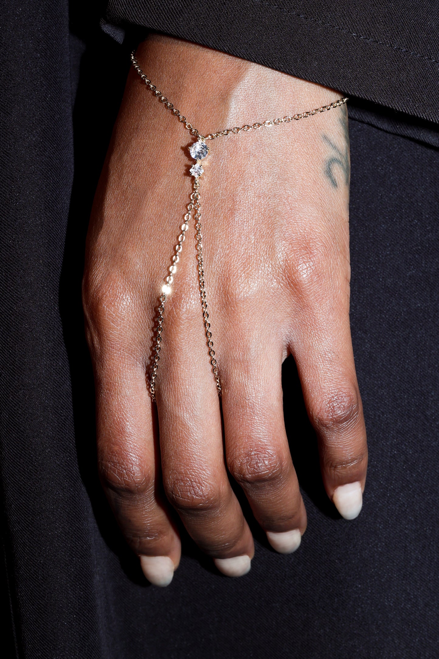 Hand wearing a delicate gold chain hand harness with diamond on a dark background