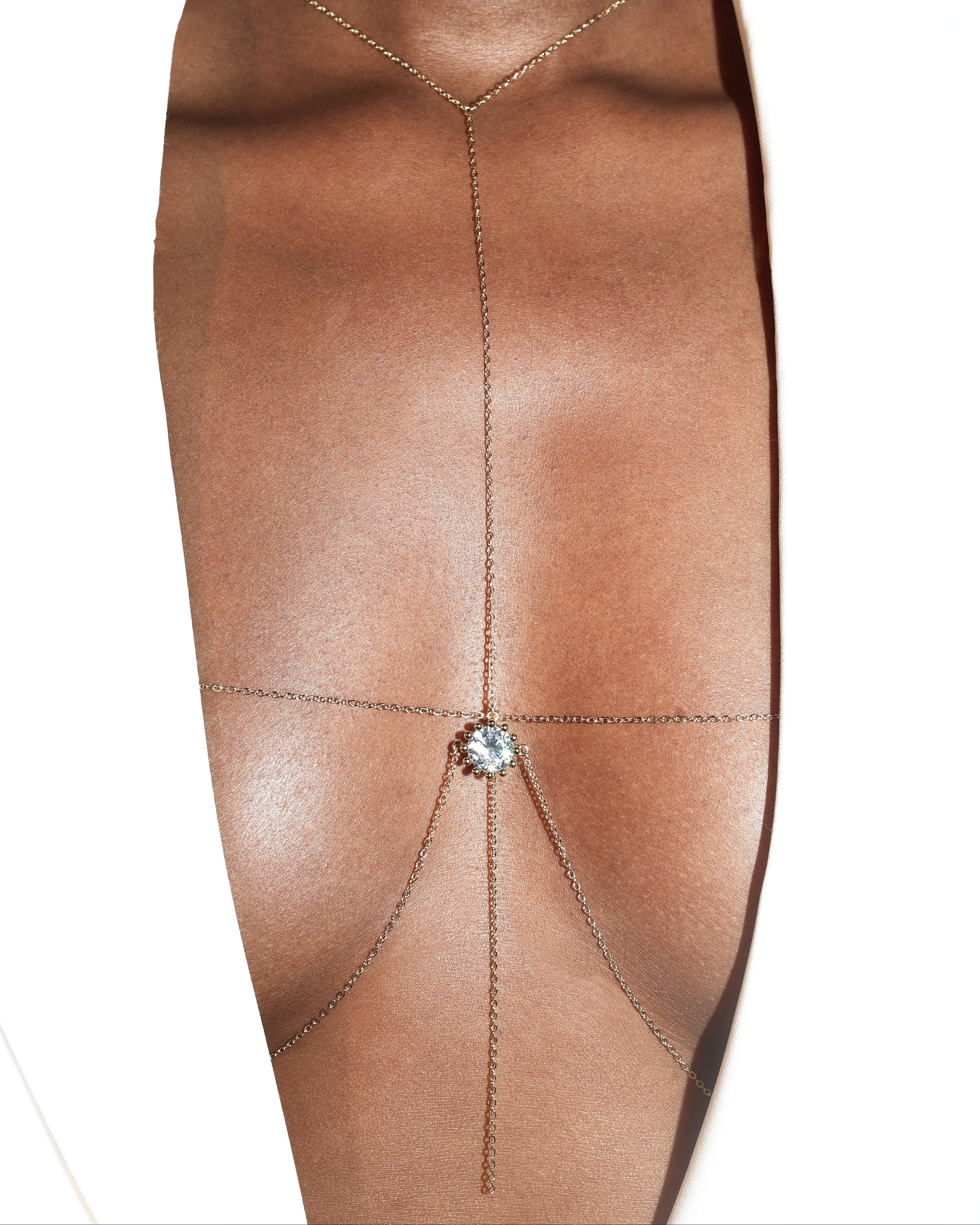 Gold delicate bra shaped body chain with round bezeled diamond centered charm on a bust with white blazer
